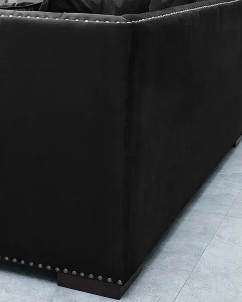 Black fabric sofa corner with silver stud detailing and wooden legs on tiled floor