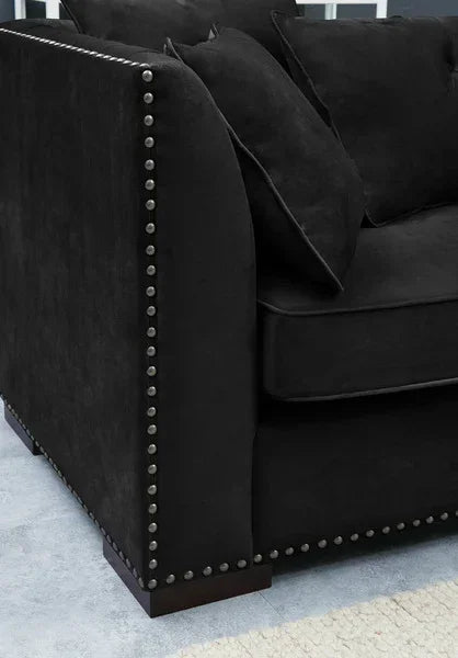 Black velvet sofa arm with silver stud detailing and scatter cushions on blue rug