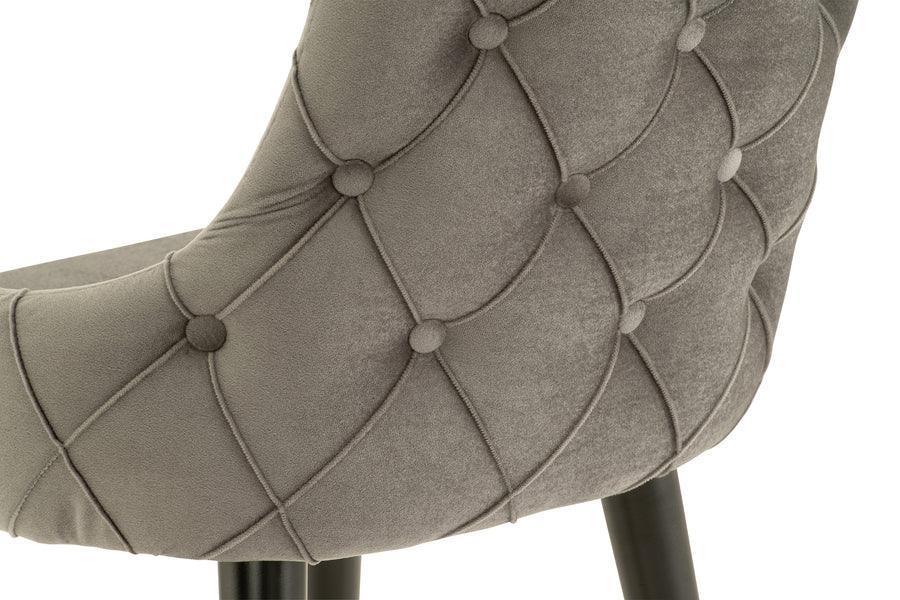 Close-up of grey velvet dining chair with button-tufted backrest and black legs