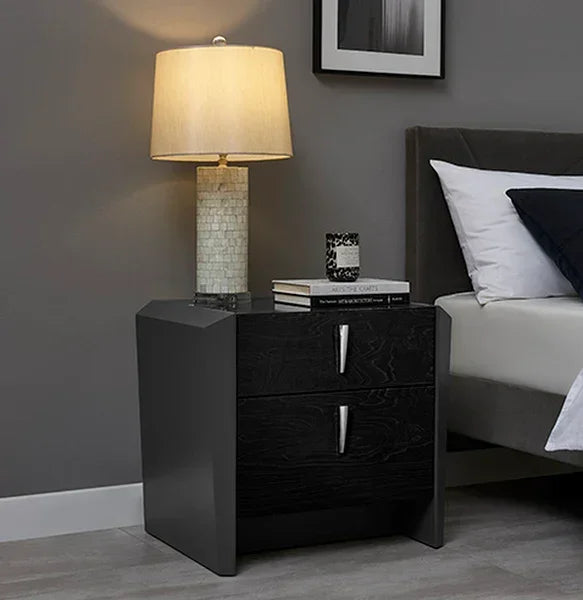 Black bedside table with two drawers beside bed, lamp and books on top