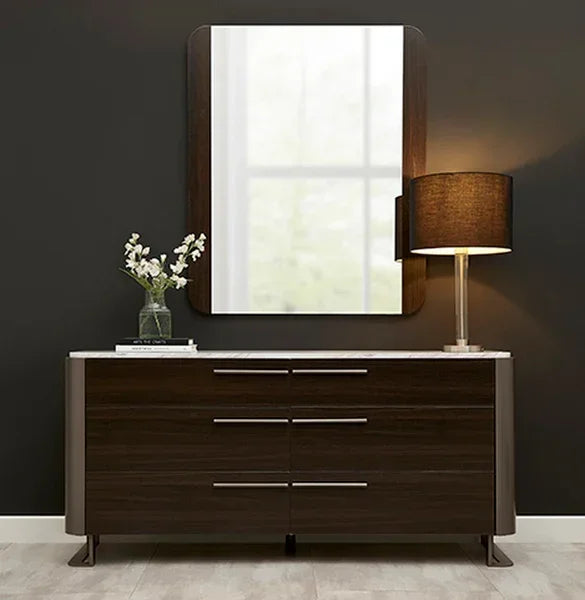 Dark wood sideboard with marble top, table lamp, and mirror against dark wall