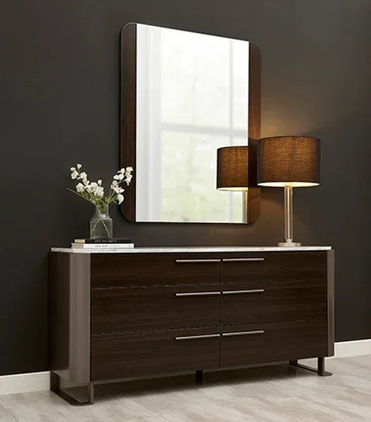 Dark wood sideboard with six drawers, marble top, table lamp, and flowers against black wall