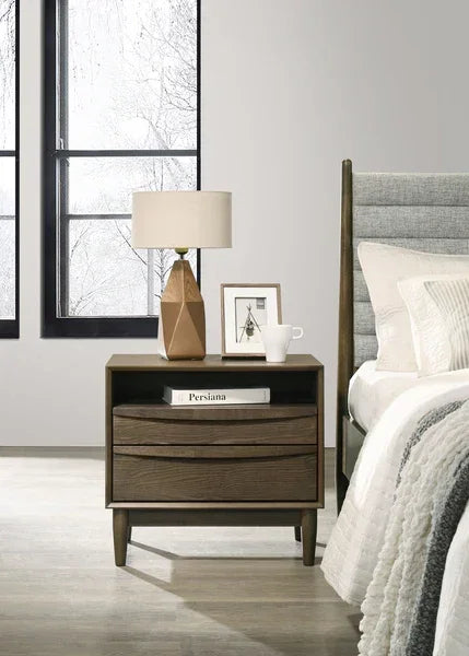 Wooden bedside table with drawers beside upholstered bed, lamp and decor on top