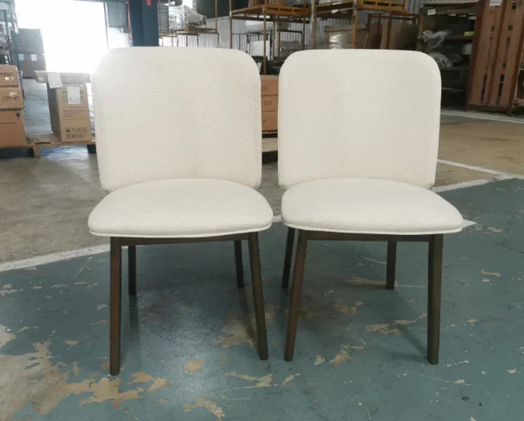 Pair of cream upholstered dining chairs with wooden legs in warehouse setting