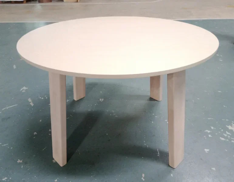 Round white wooden dining table with four legs on blue floor