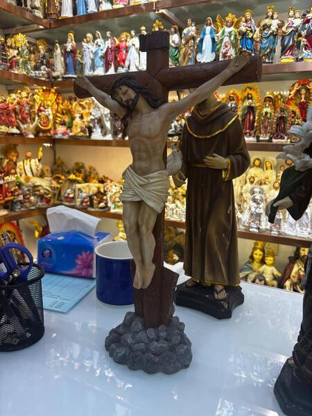 Wooden crucifix figurine of Jesus displayed on shop counter with religious statues in background