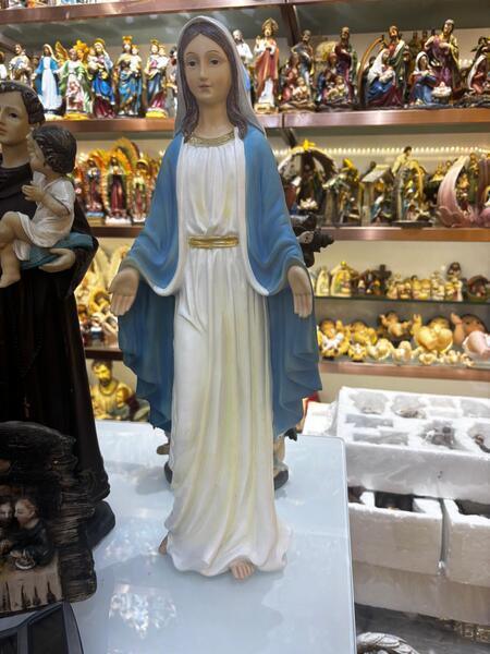 Religious figurine of a woman in white and blue robes displayed among assorted statues