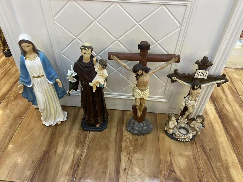Religious figurines including Virgin Mary, saint with child, and two crucifix statues on wooden floor