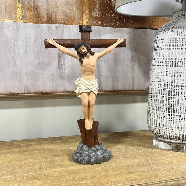 Crucifix figurine on a wooden cross with a stone-effect base, front view on a sideboard