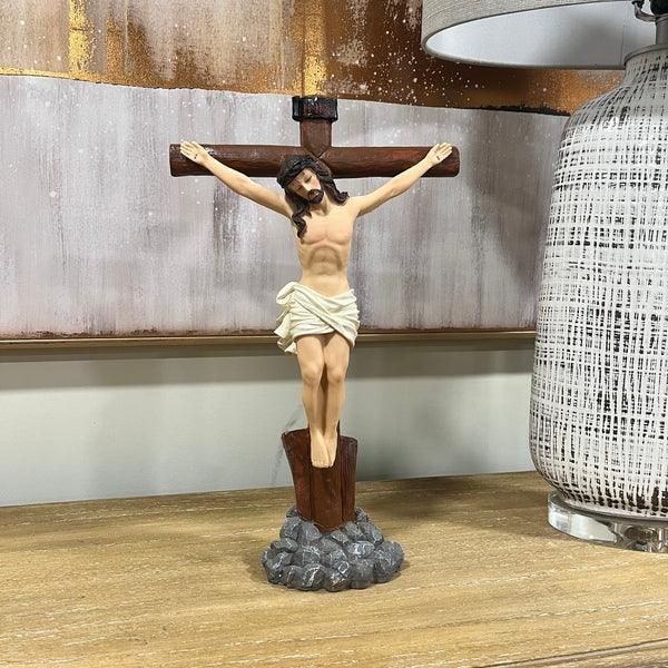 Crucifix statue on wooden base displayed next to textured ceramic lamp on table