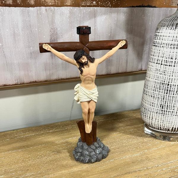 Wooden crucifix statue with Jesus figure and INRI sign on tabletop next to decorative vase
