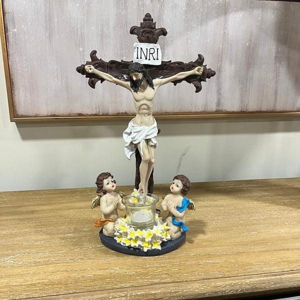 Crucifix candle holder with Jesus figure and two angel figurines on wooden table