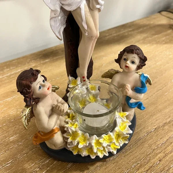 Ornamental cherub candle holder with glass cup and yellow flower accents on wooden surface
