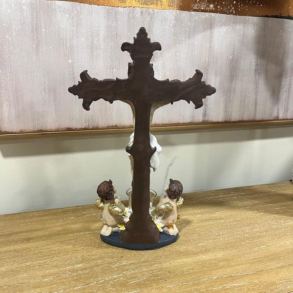 Decorative brown cross ornament with two angel figurines on wooden surface