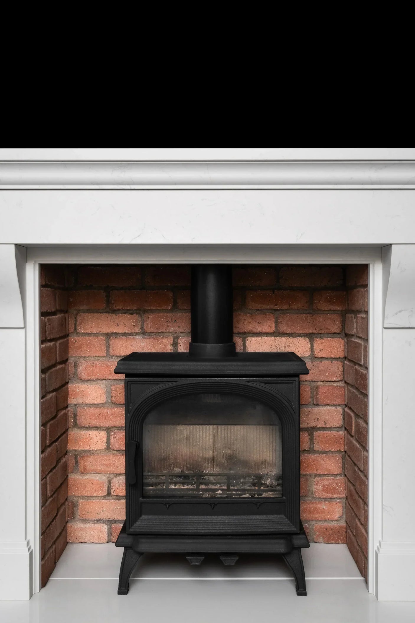 Black cast iron stove fireplace with brick surround and white mantel