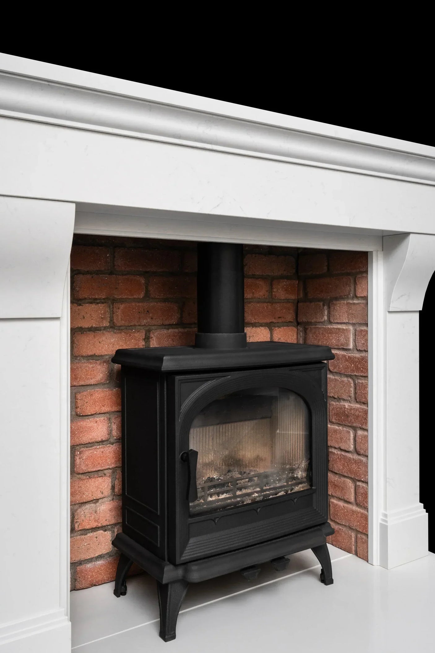 Black wood-burning stove with glass door in white fireplace surround and brick inset