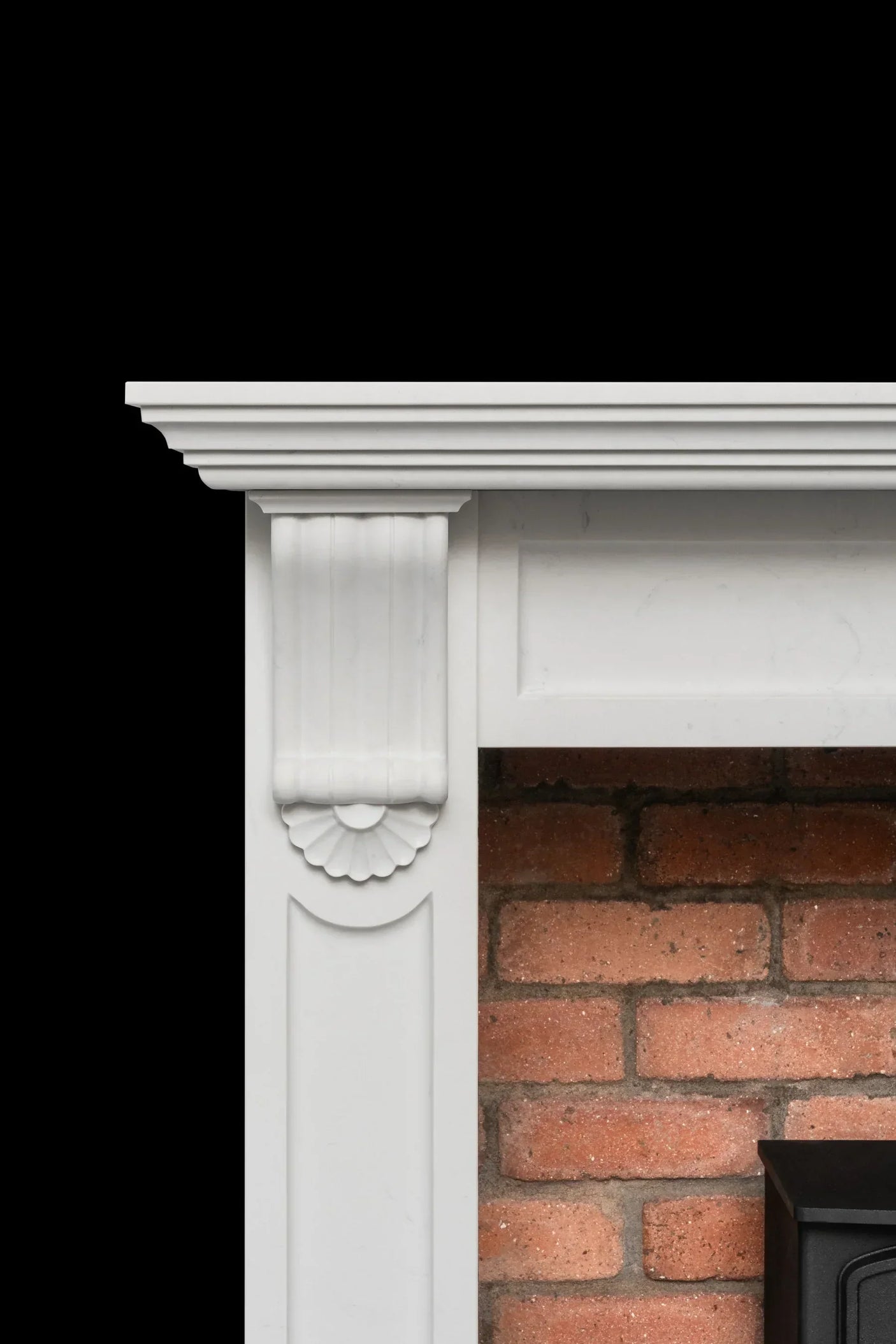 White fireplace surround with carved detailing beside red brick interior