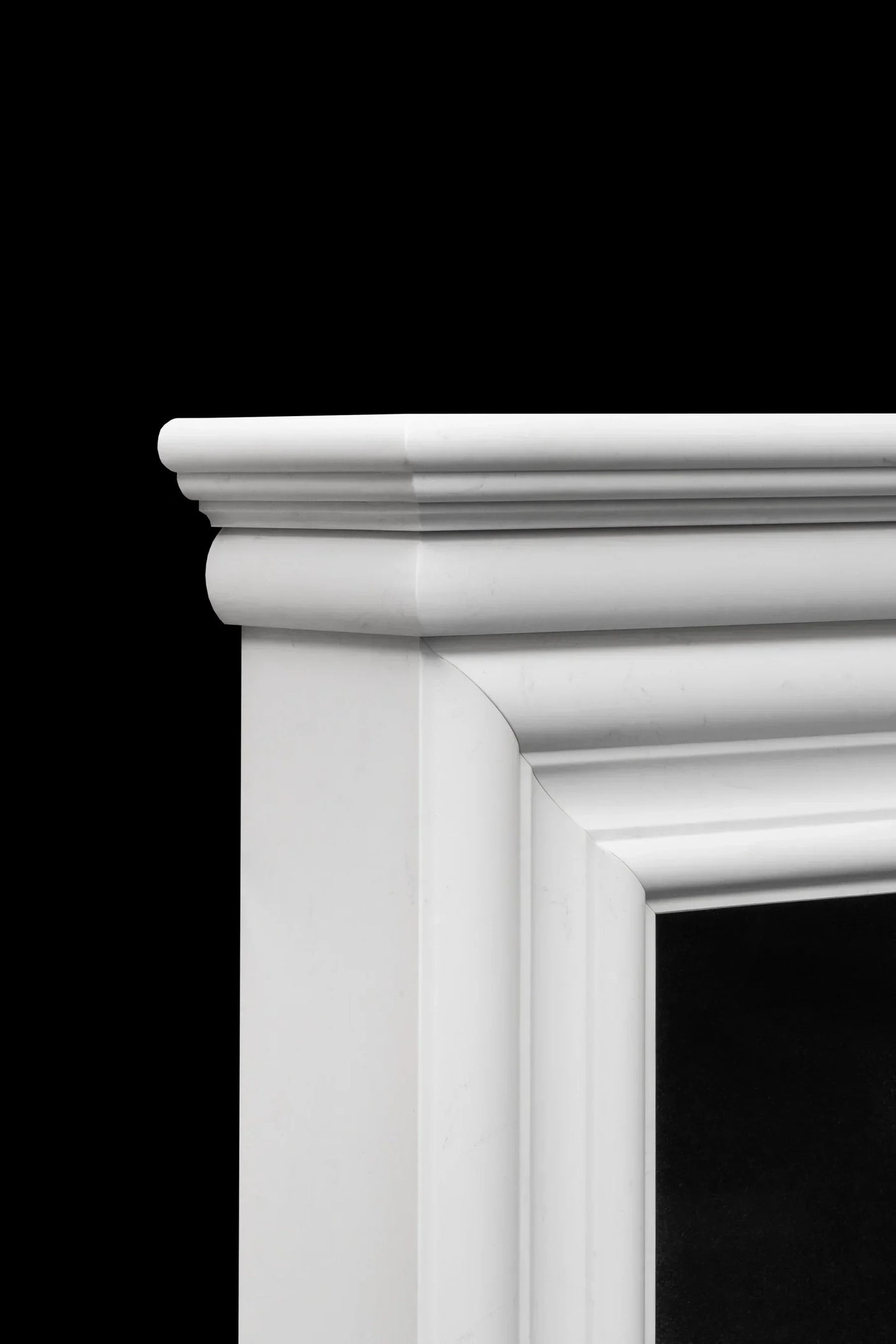 White marble fireplace mantel with detailed molding, close-up corner view against black background