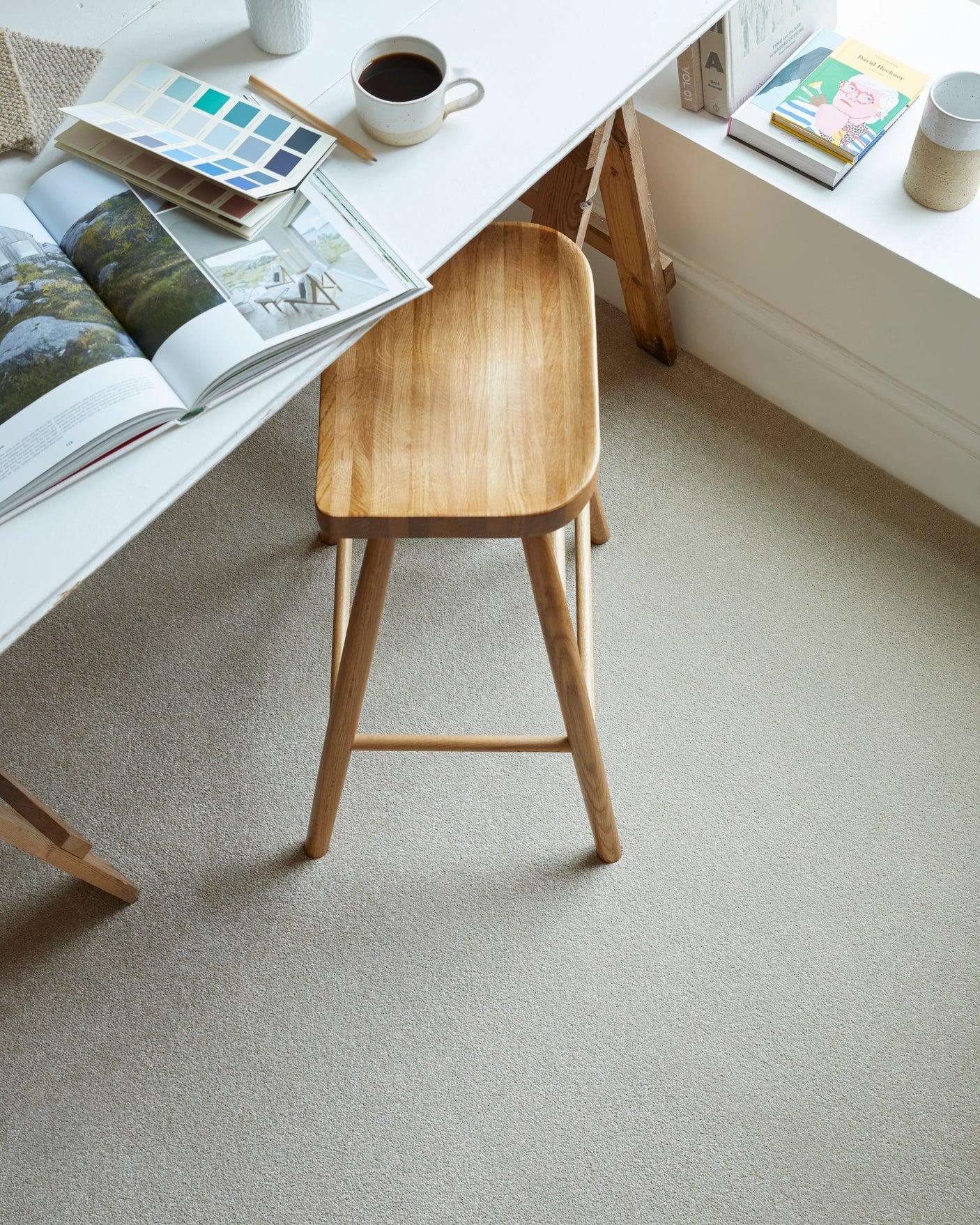 Light beige carpet in a home office with a wooden stool and open magazine on a white desk.