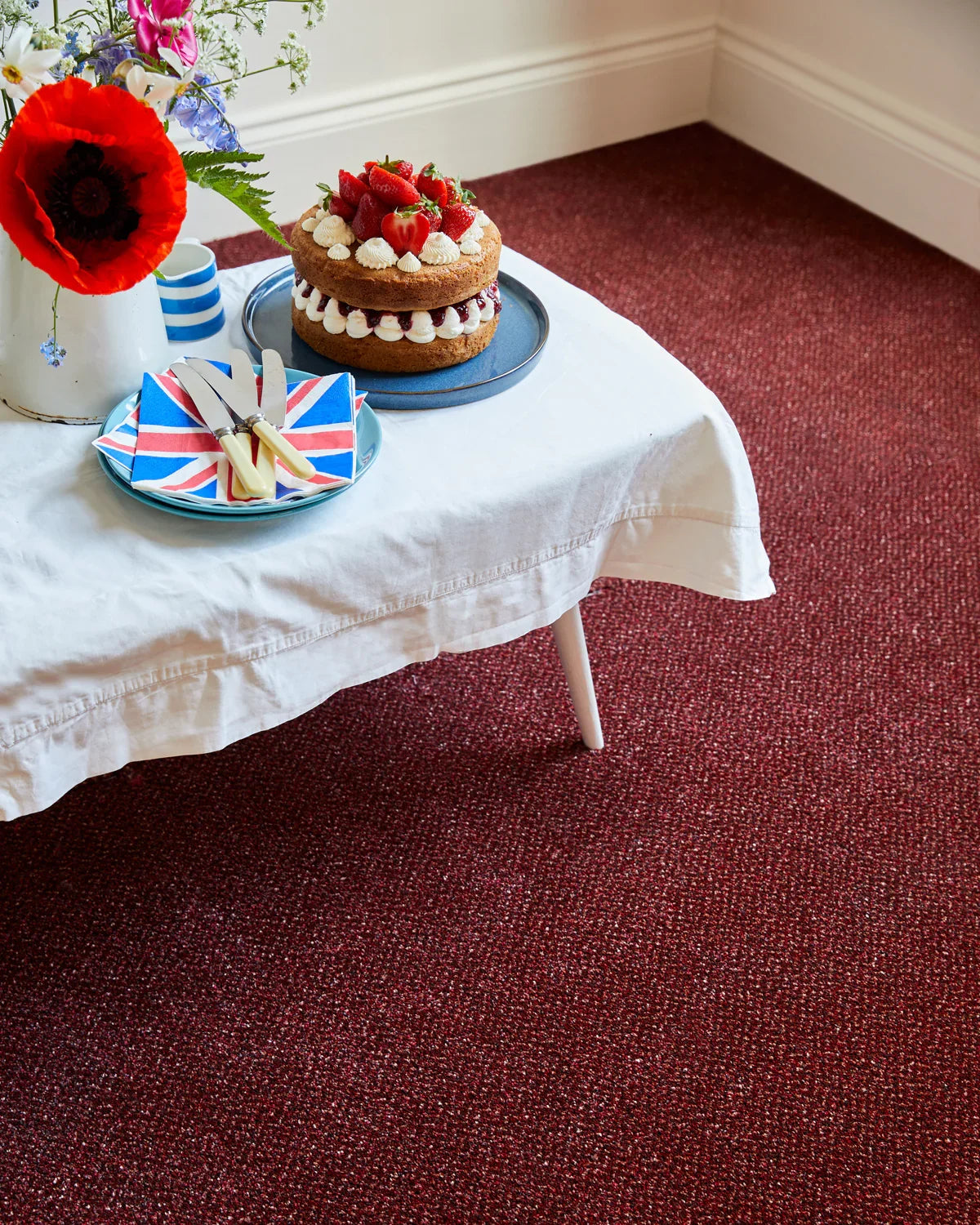 Rich burgundy carpet in dining area with cake on white tablecloth and floral decor