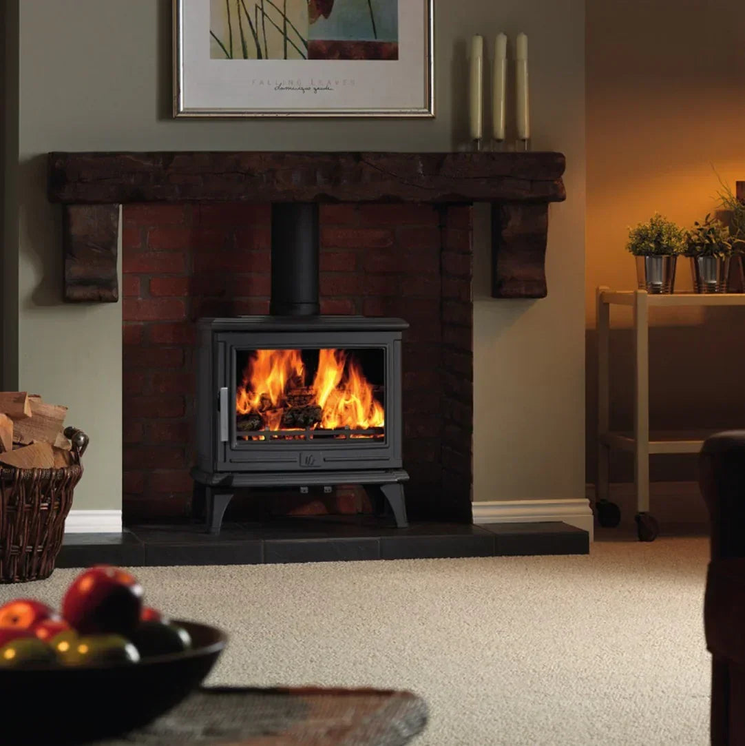 Black wood burning stove with fire in brick fireplace on beige carpeted living room floor