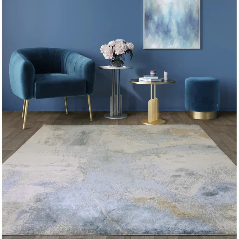 Abstract area rug in grey and cream tones styled with blue velvet chair and gold accent tables
