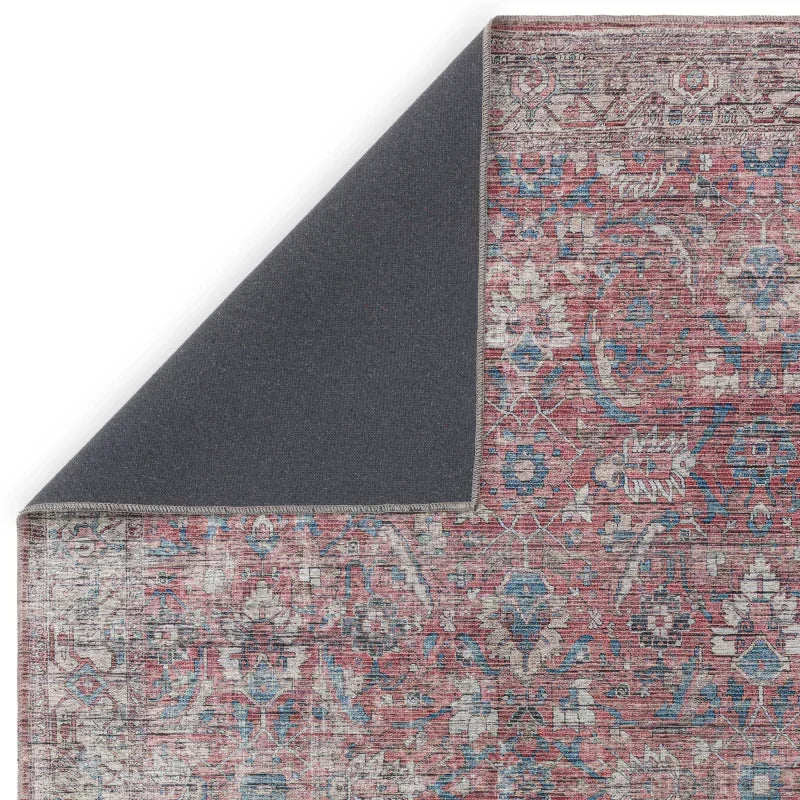 Red and blue vintage area rug with floral pattern, corner folded to show grey backing
