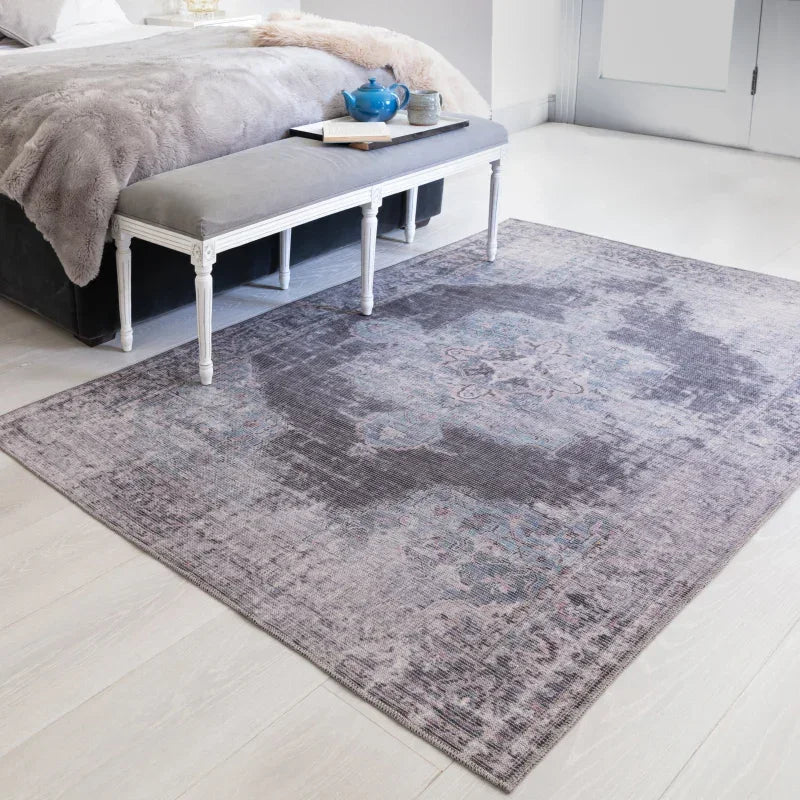 Grey patterned rug on light wood floor beside upholstered bedroom bench
