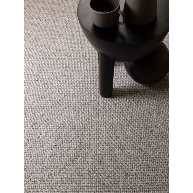 Grey textured woven rug with black modern coffee table and ceramic mug
