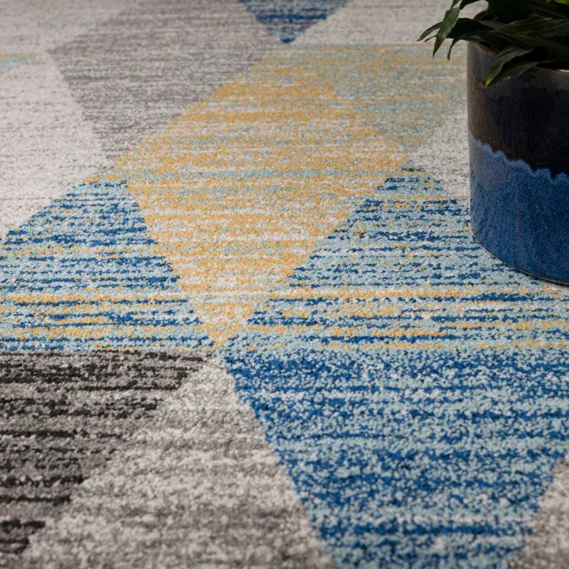Geometric patterned rug in blue, yellow, and grey with plant pot on textured surface