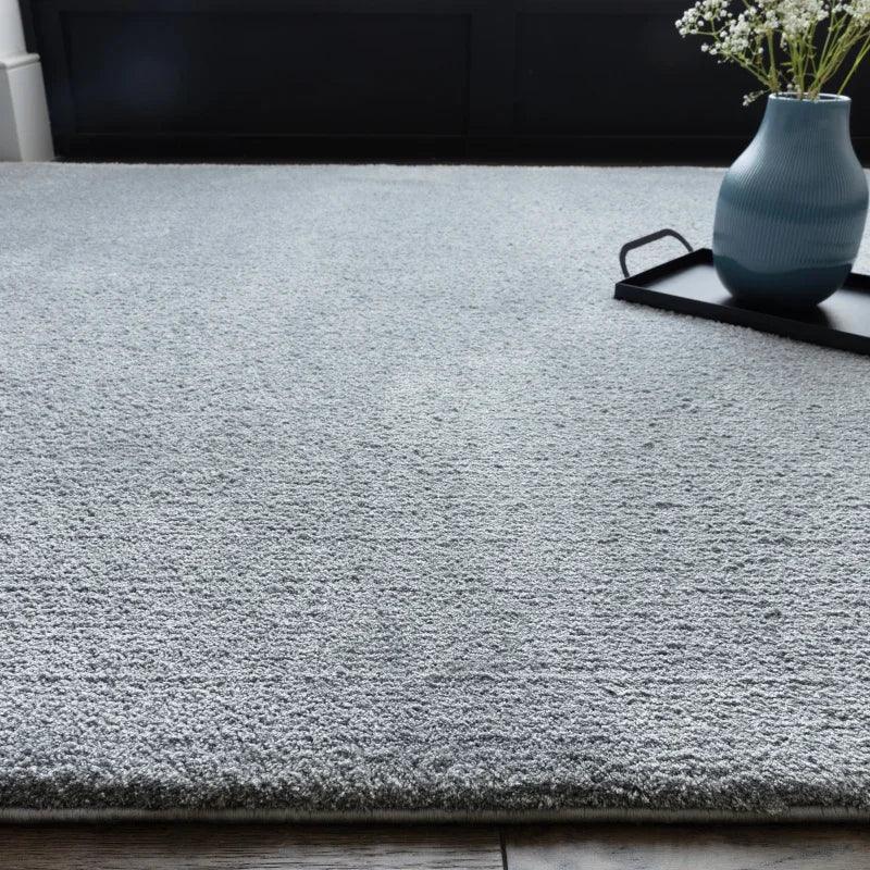 Light grey area rug on wooden floor with decorative vase on tray