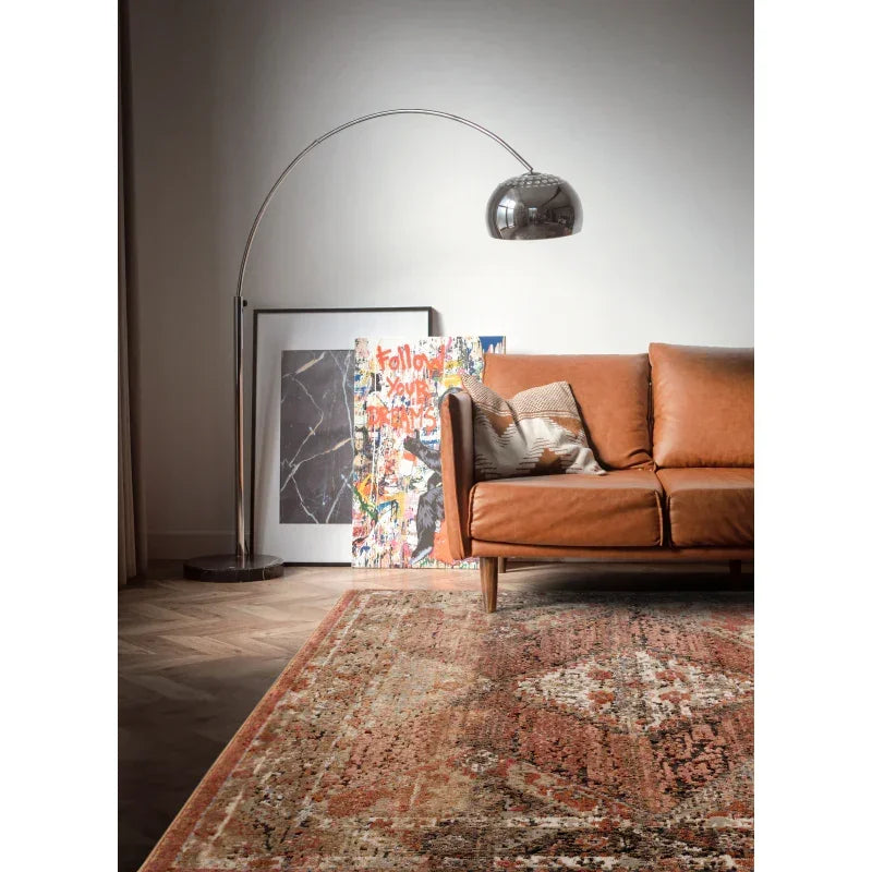 Tan leather sofa with scatter cushion, modern floor lamp, and patterned rug in living room