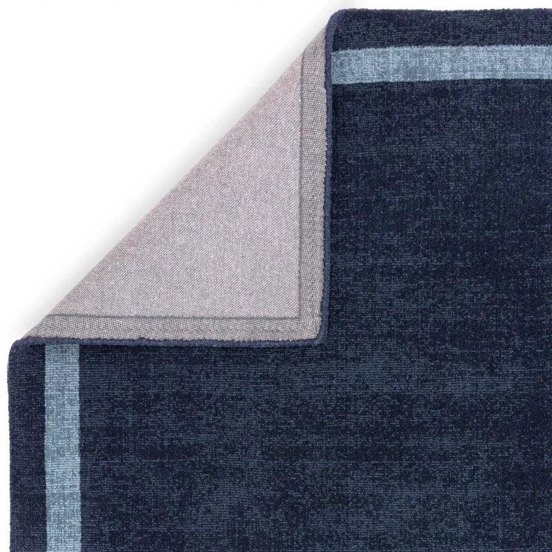 Navy blue area rug with light blue border, corner folded to show backing detail