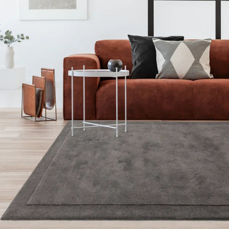 Brown sofa with black and white cushions, grey area rug, and white side table in living room