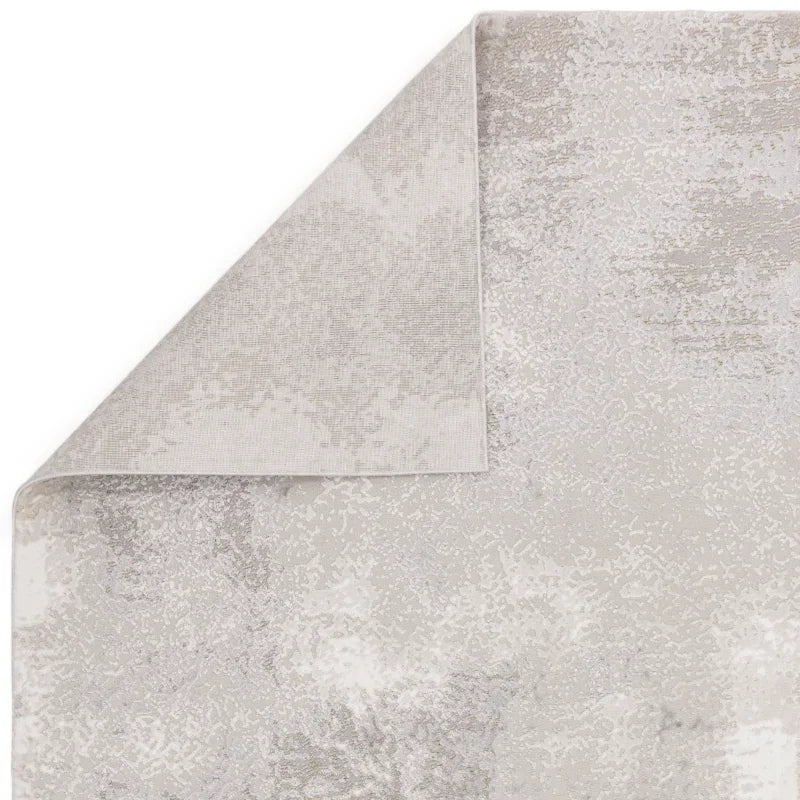 Light grey patterned area rug with one corner folded to show backing texture