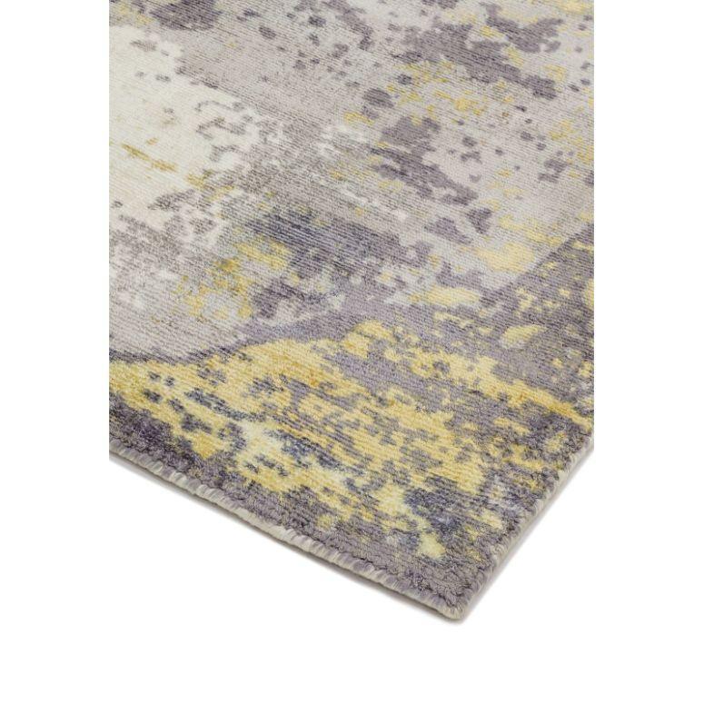 Abstract area rug with grey, yellow, and cream tones shown in close-up corner view