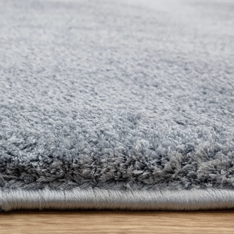 Closeup of light grey shaggy rug on wooden floor, showing thick pile texture