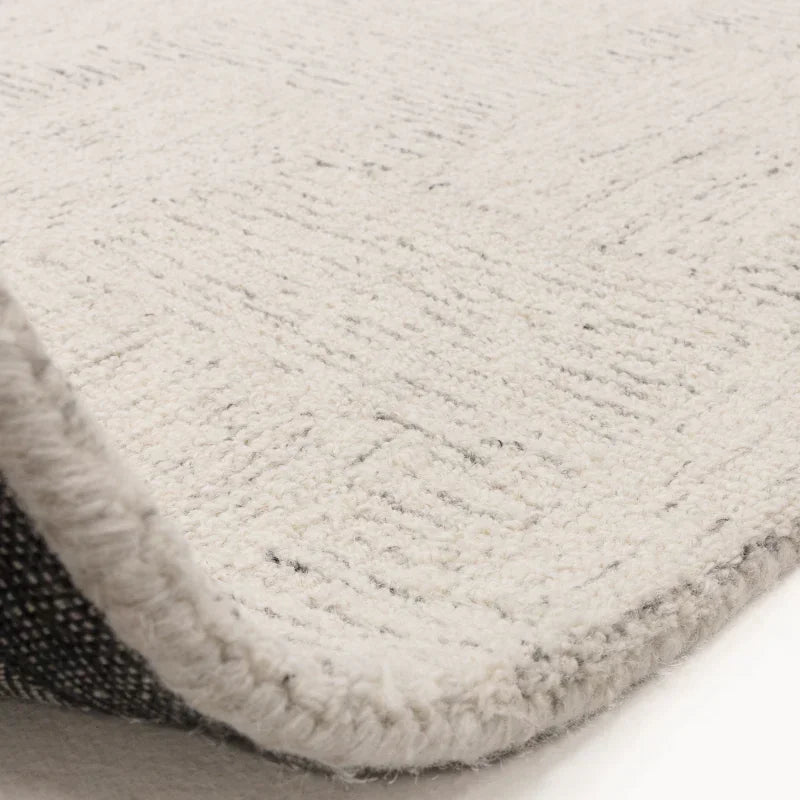 Close-up of cream textured rug with woven edge and subtle grey pattern detail