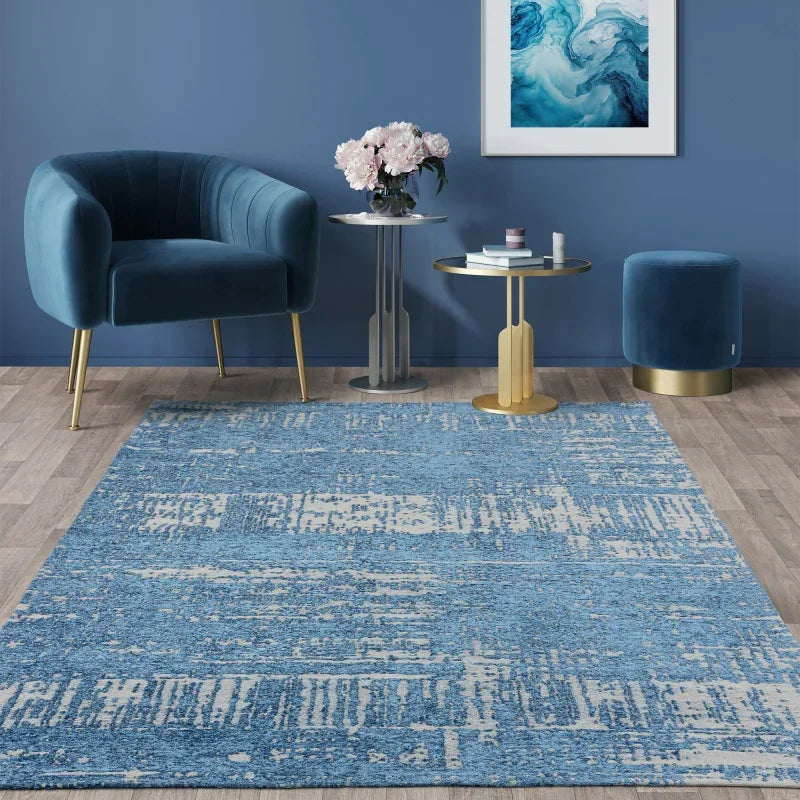 Blue abstract rug in modern living room with velvet chair, ottoman, and gold accent tables