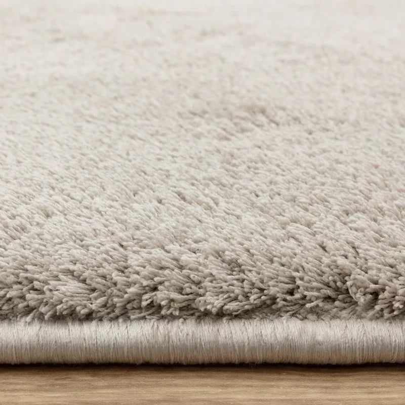 Close-up of beige shaggy rug pile and edge on wooden floor