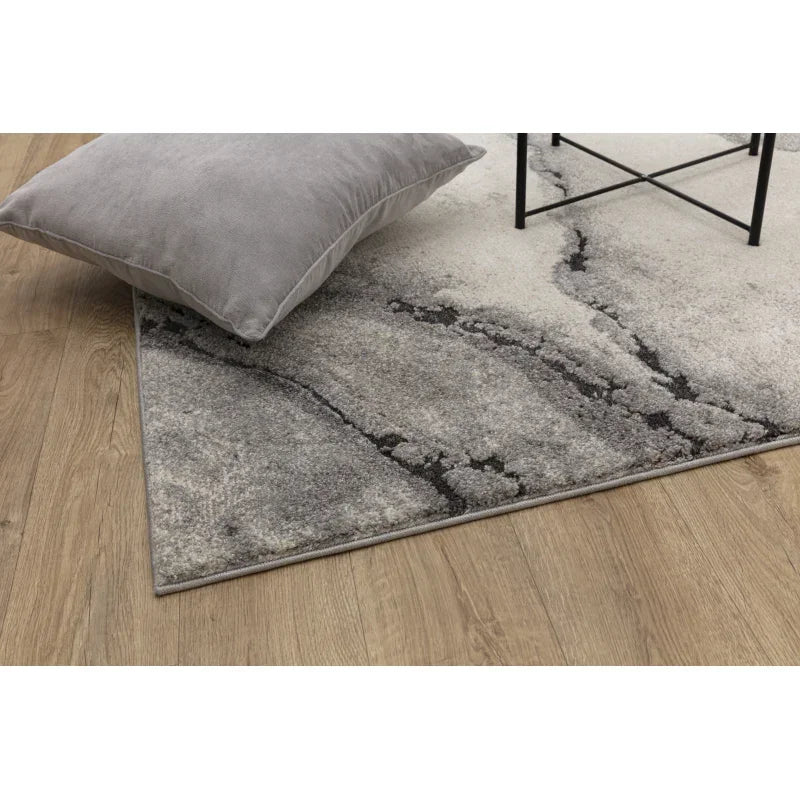 Grey abstract area rug with cushion on wooden floor, modern living room decor