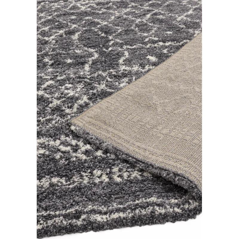 Grey shaggy area rug with geometric pattern and visible corner showing backing