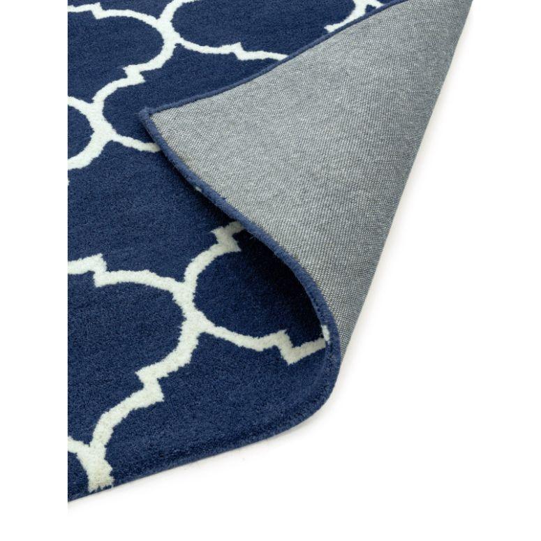 Navy blue geometric rug with white trellis pattern, corner folded to show backing