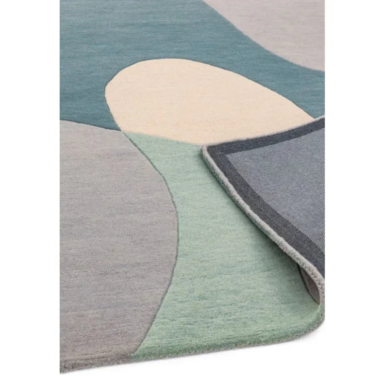 Abstract wool rug with blue, green and beige shapes, corner folded to show backing