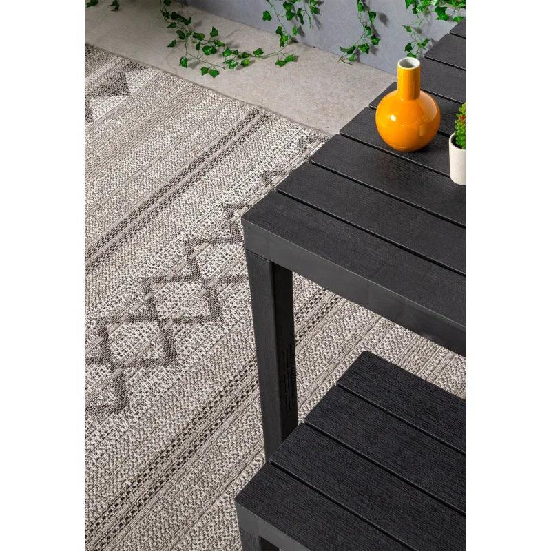 Black slatted dining table and bench with orange vase on geometric patterned rug