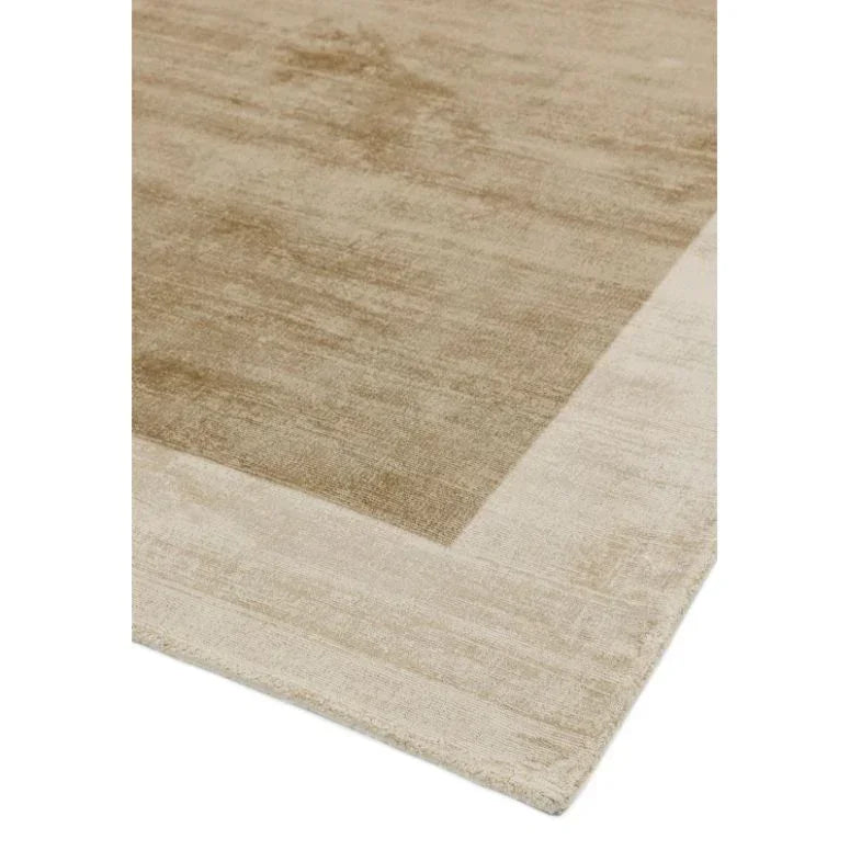Beige area rug with wide light border and soft textured finish, corner angle view