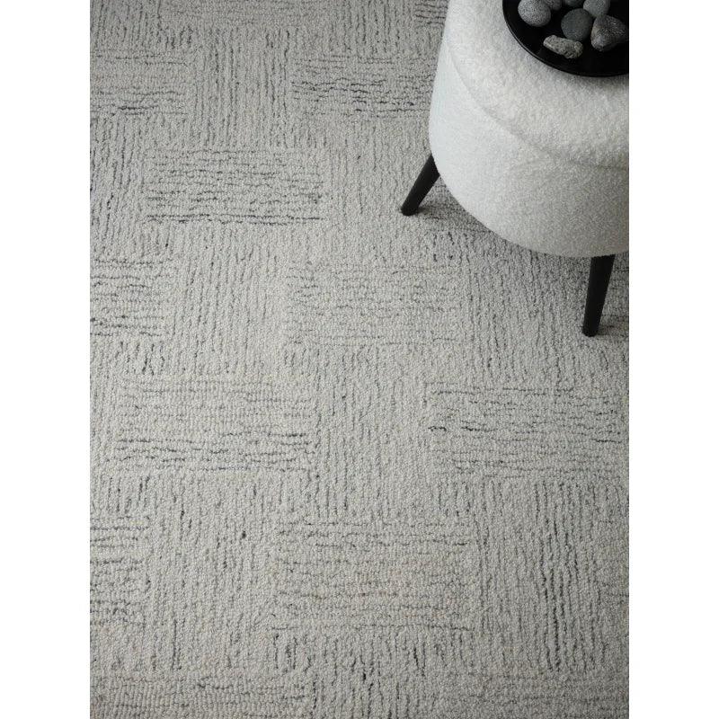 Light grey textured rug with geometric pattern beneath a round upholstered stool