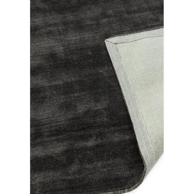 Corner detail of dark grey area rug with fabric backing and texture visible