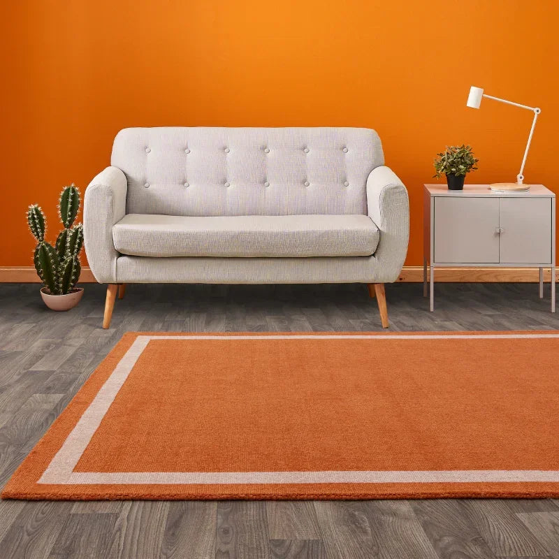 Grey fabric sofa with wooden legs and orange rug in modern living room