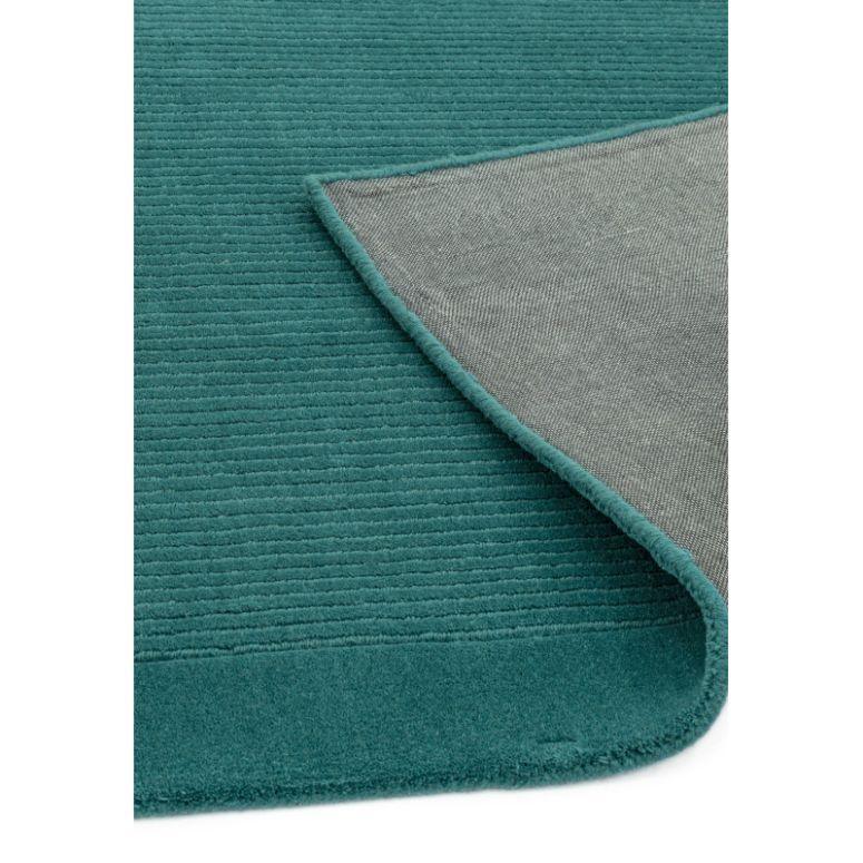 Teal area rug with ribbed texture and finished border, corner lifted to show backing